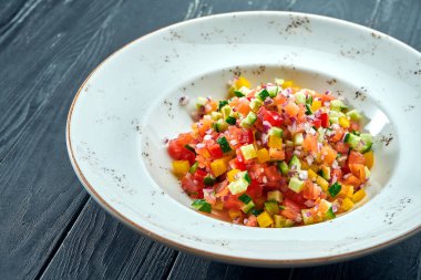 Sebze salatası, domates, biber, salatalık ve soğan ile birlikte koyu ahşap arka planda beyaz bir tabakta. Sebze salatası