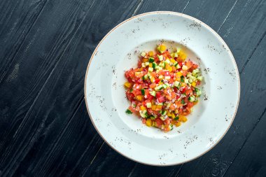 Sebze salatası, domates, biber, salatalık ve soğan ile birlikte koyu ahşap arka planda beyaz bir tabakta. Sebze salatası