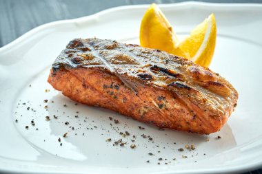 Limonlu mangal kömürlü ızgara somon bifteği. Koyu ahşap arka planda beyaz tabakta servis ediliyor. Barbekü deniz ürünleri.