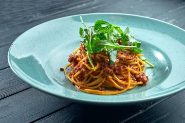 Geleneksel makarna, kıymalı makarna ve roka soslu domates, siyah ahşap arka planda mavi bir tabakta servis ediliyor. İtalyan mutfağı