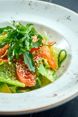 İştah açıcı, salatalı diyet salatası, salatalık, avokado ve koyu ahşap arka planda beyaz tabakta hafif tuzlanmış somon. Sağlıklı yemek.