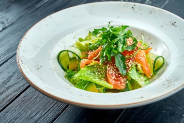 İştah açıcı, salatalı diyet salatası, salatalık, avokado ve koyu ahşap arka planda beyaz tabakta hafif tuzlanmış somon. Sağlıklı yemek.