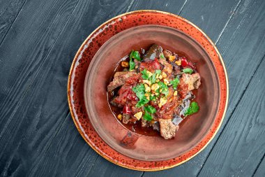 Kil içinde patlıcanlı, fındıklı, domatesli ve kişniş ile pişirilmiş biftek, siyah arka planda bir kasede servis edilir. Restoran yemekleri..