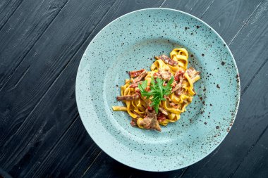 Geleneksel makarna sosisli, biftekli ve domatesli makarna, roka, siyah, ahşap arka planda mavi bir tabakta servis edilir. İtalyan mutfağı