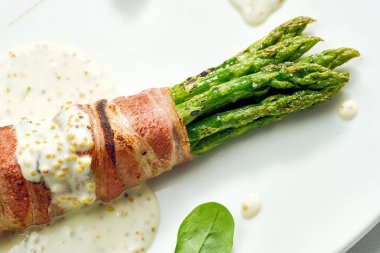 Pastırmalı ızgara kuşkonmaz ve beyaz tabakta hardal sosu. Beyaz arkaplanda izole.