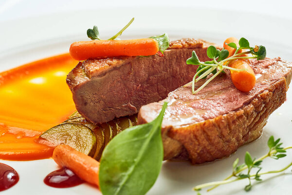 Appetizing confit duck breast with pear and yellow apple puree, berry sauce in a white plate. Isolated on grey background.