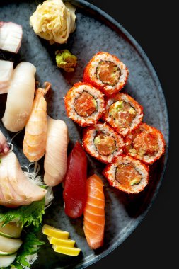 Çeşitli nigirilerden oluşan iştah açıcı bir suşi seti. Somon, avokado ve tobiko havyarlı saşimi ve uramaki. Geleneksel Japon mutfağı. Yemek servisi. Siyah üzerine izole edilmiş.