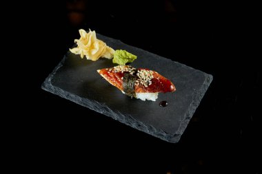 Zencefil ve wasabi ile siyah tahtada yılan balığı ve unagi soslu Nigiri suşisi. Japon mutfağı. Yemek servisi. Siyah üzerine izole edilmiş.