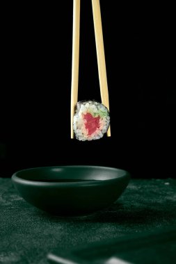 Maki suşisi ve somon. Klasik Japon mutfağı. Yemek servisi. Siyah arka plan. Çubuklar sushi tutar