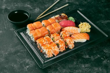 Somon, avokado, tobiko havyar ve nigiri ile çeşitli uramaki çeşitlerinden oluşan iştah açıcı bir suşi seti. Geleneksel Japon mutfağı. Yemek servisi. Siyah arkaplan