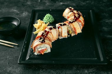 Suşi, arka planda siyah bir tabakta yılan balığı ve somon balığıyla altın bir ejderha sarar. Yemek servisi. Japon mutfağı.