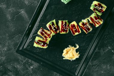 Siyah bir arka planda siyah bir tabakta avokado, yılan balığı ve tobiko havyarlı suşi dürümü yeşil ejderhası. Yemek servisi. Japon mutfağı.