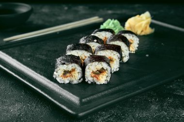 Siyah bir arka planda siyah bir tabakta yılan balıklı suşi rulosu. Yemek servisi. Japon mutfağı