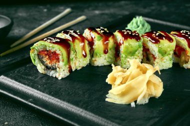 Siyah bir arka planda siyah bir tabakta avokado, yılan balığı ve tobiko havyarlı suşi dürümü yeşil ejderhası. Yemek servisi. Japon mutfağı.