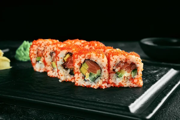 Uramaki sushi california roll in tobiko caviar with salmon, avocado and cucumber. Classic Japanese cuisine. Food delivery.