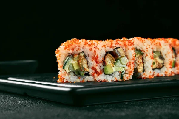 Uramaki sushi california roll in tobiko caviar with eel, avocado and cucumber. Classic Japanese cuisine. Food delivery. Isolated on white.