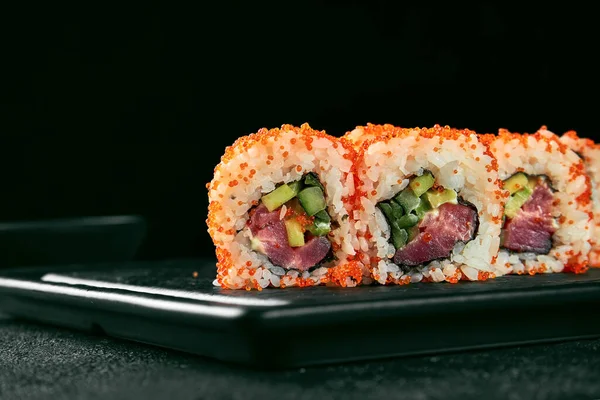 Uramaki sushi california roll in tobiko caviar with tuna, avocado and cucumber. Classic Japanese cuisine. Food delivery. Isolated on white.