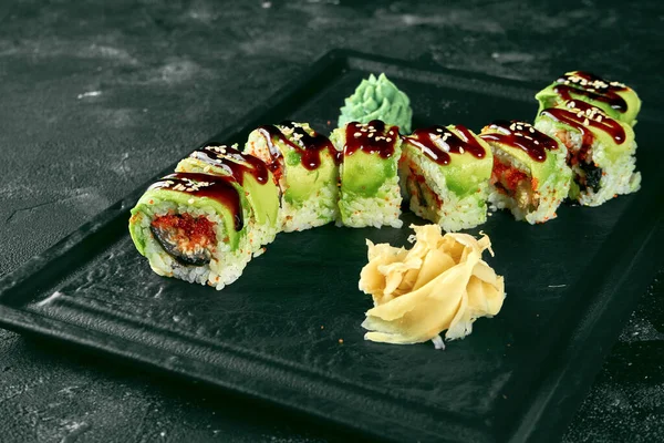 Siyah bir arka planda siyah bir tabakta avokado, yılan balığı ve tobiko havyarlı suşi dürümü yeşil ejderhası. Yemek servisi. Japon mutfağı.