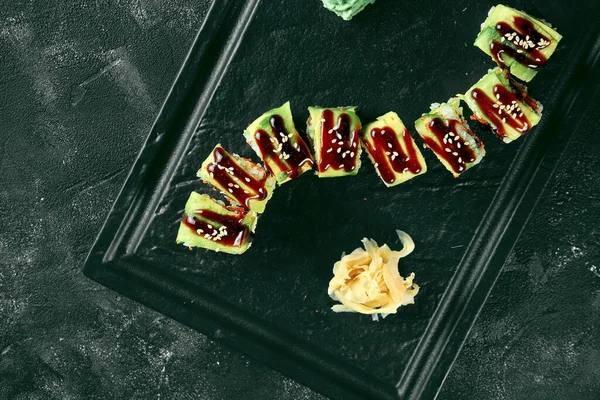 Siyah bir arka planda siyah bir tabakta avokado, yılan balığı ve tobiko havyarlı suşi dürümü yeşil ejderhası. Yemek servisi. Japon mutfağı.