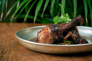 Izgara tavuk bacağı, beyaz barbekü soslu panzu salatalığı ve ahşap bir arka planda bir tabakta sos.