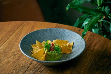 Meksika avokado guacamole ile nacho, acı biber ve fesleğen gri tabakta.