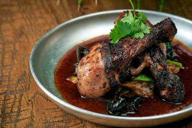 Izgara tavuk bacağı, beyaz barbekü soslu panzu salatalığı ve ahşap bir arka planda bir tabakta sos.