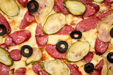 Salamlı, salatalıklı, zeytinli, soslu, erimiş peynirli, gevrek kenarlı, beyaz arka planda izole edilmiş pizza.