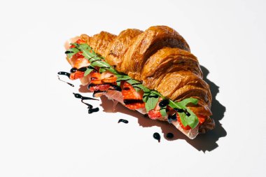 Prosciutto, çilek, roka ve balzamik soslu kruvasan sandviçi. Sert ışık. Beyaz arkaplan