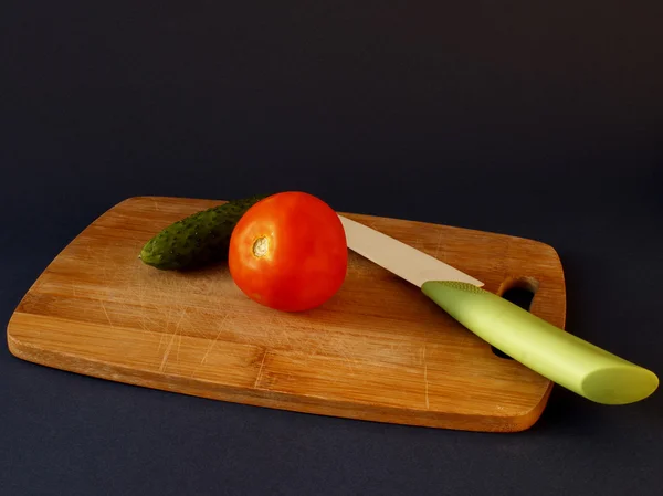 Concombre vert et tomate rouge avec un couteau sur une planche à découper Images De Stock Libres De Droits