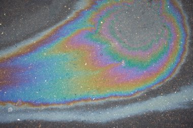 Soyut gökkuşağı etkisi, ıslak asfaltta renkli gaz lekesi. Yaya kaldırımındaki bir arabadan sonra gökkuşağı benzin sızıntısı..