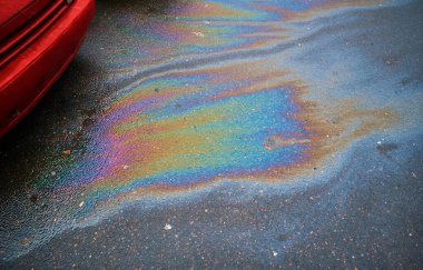Islak asfaltta renkli gaz lekesi. Arabanın altındaki sızıntıdan kaynaklanan yağ lekesi. Çevre kirliliği kavramı..