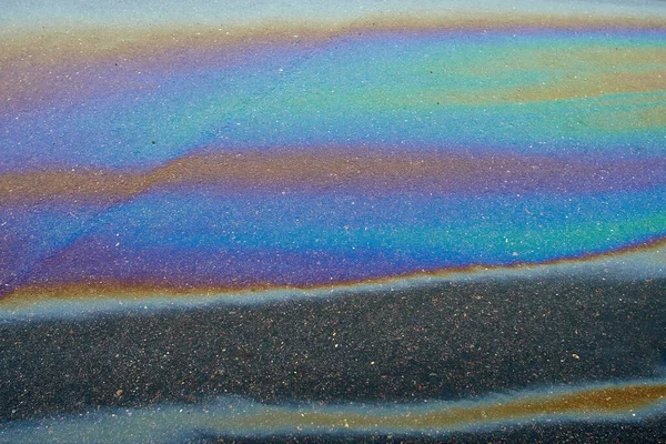 Abstract rainbow effect, colorful gas stain on wet asphalt.Rainbow gasoline leak after a car on a pedestrian sidewalk.