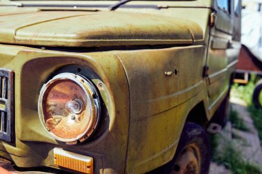 Kırık farlı, eski, paslı bir arabanın ön tarafı.