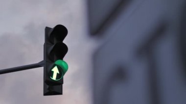 Bulutlu bir gökyüzüne karşı bir trafik ışığı yeşil, turuncu ve kırmızıyla aydınlatılır. Hareket gösteren ok.