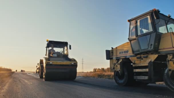 Novosibirsk bölgesi, 4 Eylül 2020. Yol yüzeyi tamiri. Yeni bir yol inşaatı. Patenler gün batımında asfaltı düzleştirir ve sıkıştırır. Taze asfalt. — Stok video