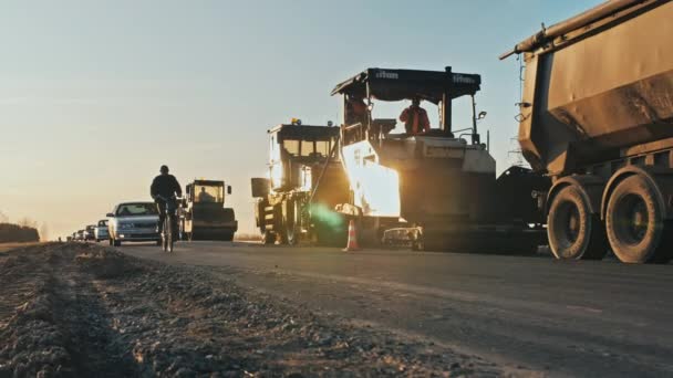 Gebiet Nowosibirsk, 4. September 2020. Straßenreparaturen. Straßenbaumaschinen. Asphaltfertiger, Walzen. Vorbei an Radfahrern und Autos. Blendung und Reflexionen der untergehenden Sonne. — Stockvideo