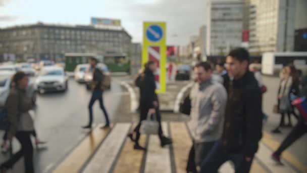 Objektivunschärfe, unscharf. Eine Menschenmenge von Fußgängern überquert die Straße vor dem Hintergrund von Autos auf nassem Asphalt nach Regen. Gedrängter Fußgängerüberweg. — Stockvideo