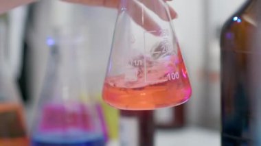 Yakın plan. Laboratuvar kimyacısı tarifleri hacimli bir şişede karıştırıyor. Aşı Araştırma Laboratuvarı.