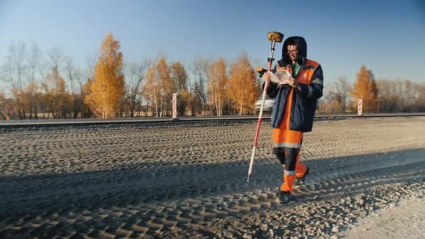 Novosibirsk region, 3 augusti 2020. En manlig lantmätare gör mätningar, verifierar data. Geodetiska verk. Navigationssystem. Anläggning av en ny motorväg. — Stockvideo