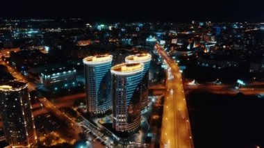 Hava görüntüsü. Şehrin arka planına karşı üç güzel aydınlatılmış eve uçuş. Şehir merkezinde otoyol. Şehir hayatı.