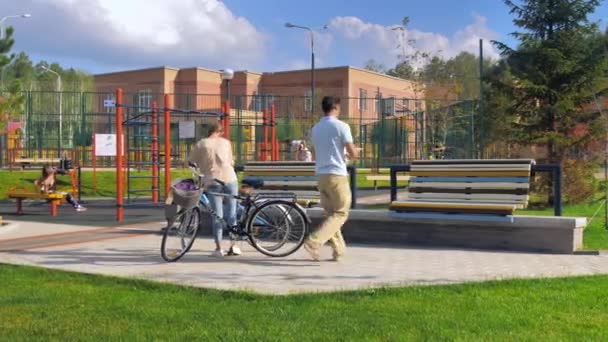 Pareja joven y feliz se detuvo a descansar en un banco después de andar en bicicleta en un día soleado de verano. El hombre le lanza helado a la mujer. Humor lúdico, estilo de vida activo, romance, felicidad. — Vídeos de Stock