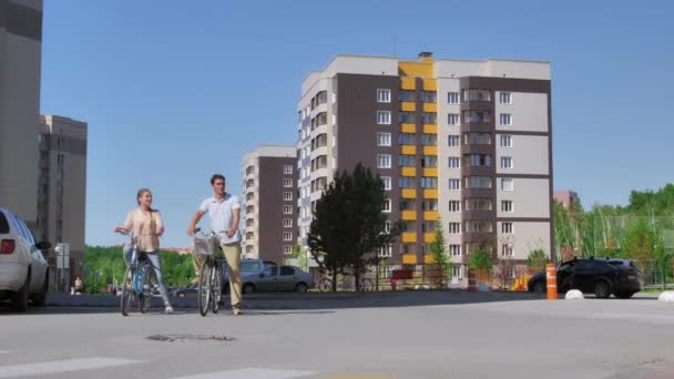 Новосибирск, 15 июля 2019 года. Счастливая молодая пара на велосипедах скучает по детям, идущим по пешеходному переходу. Дети ходят парами, держась за руки. Женщина и маленькая девочка машут друг другу. — стоковое видео