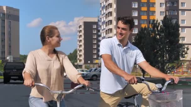 Pareja feliz en bicicletas intercambian miradas, sonriendo. La mujer saluda saludando con la mano. Ciclismo, romance, amor. Día soleado de verano, estilo de vida. — Vídeo de stock