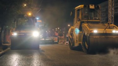 Novosibirsk bölgesi, 7 Eylül 2019. İki yol silindiri geceleyin asfaltı sıkıştırır. Arka planda asfalt kaldırım taşı. Taze asfalttan çıkan buhar. Yol yüzeyi onarımı.