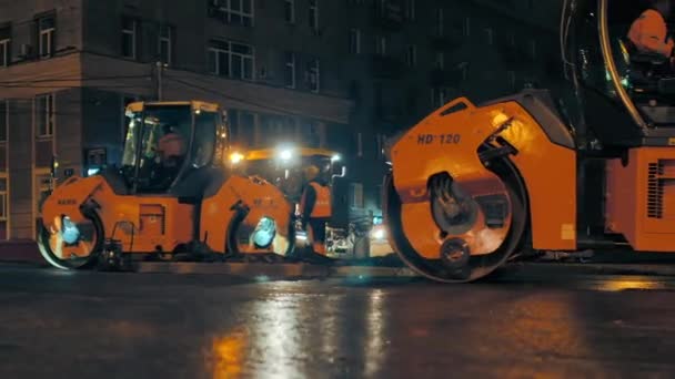 Gebiet Nowosibirsk, 7. September 2019. Zwei Straßenwalzen verdichten den Asphalt vor dem Hintergrund der nächtlichen Lichter der Stadt. Im Hintergrund Asphaltfertiger. Fahrbahnsanierung. — Stockvideo