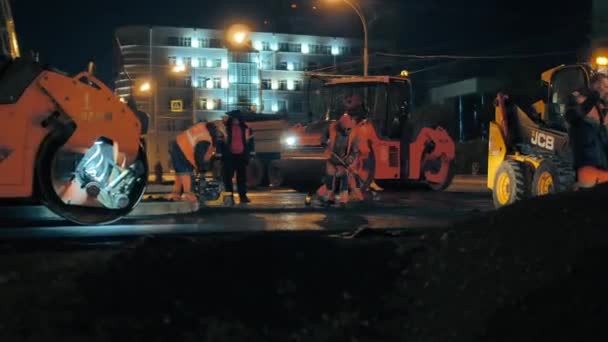 Gebiet Nowosibirsk, 7. September 2019. Straßenarbeiter verteilen Asphaltmischung für eine Straßenwalze. Straßenwalzen verlegen Asphalt. Reparatur einer Stadtstraße in der Nacht. — Stockvideo