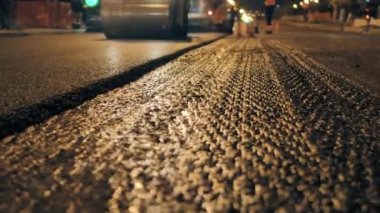 Şehirde yeni asfalt döşenmiş bir tabaka. Gece yol tamiri. Yol silindiri asfalt seriyor. Yeni bir yol inşaatı.