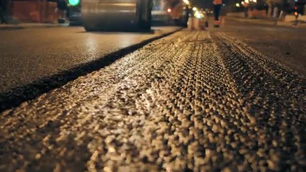 Eine Schicht frisch verlegten Asphalts in der Stadt. Straßenreparaturen in der Nacht. Die Straßenwalze verlegt Asphalt. Bau einer neuen Straße. — Stockvideo