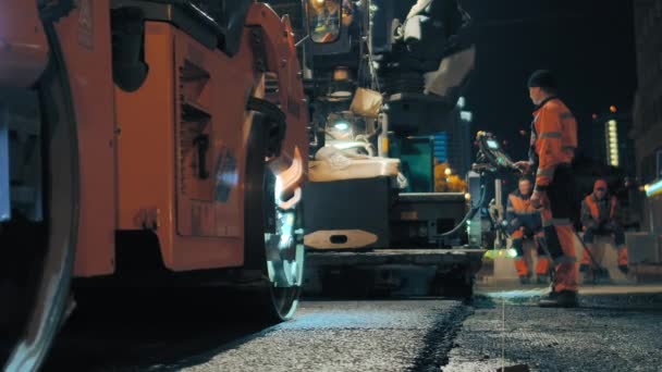 Novosibirsk região, 7 de setembro de 2019. Um trabalhador rodoviário no painel de controle do paver paver controla o trabalho. O rolo de estrada está colocando asfalto. Reparação de uma estrada de cidade à noite. — Vídeo de Stock