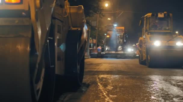 Zwei Straßenwalzen verdichten den Asphalt vor einem Asphaltfertiger. Reparatur einer Stadtstraße in der Nacht. Dampf aus heißem Asphalt. — Stockvideo